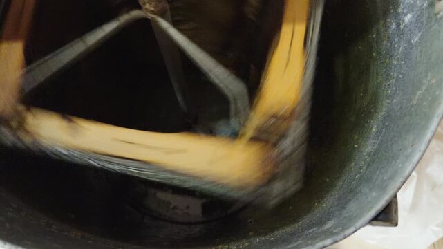 Slow-motion close-up of honey flowing inside a rotating extractor machine during traditional beekeeping and honey extraction process.