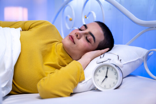Young short haired woman sleeping in bed and reaching to turn off alarm clock in the morning