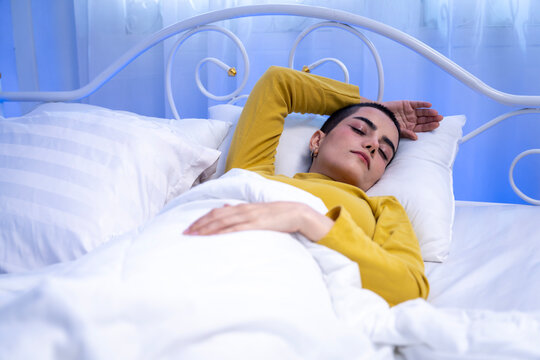 Young short haired woman sleeping in bed and reaching to turn off alarm clock in the morning