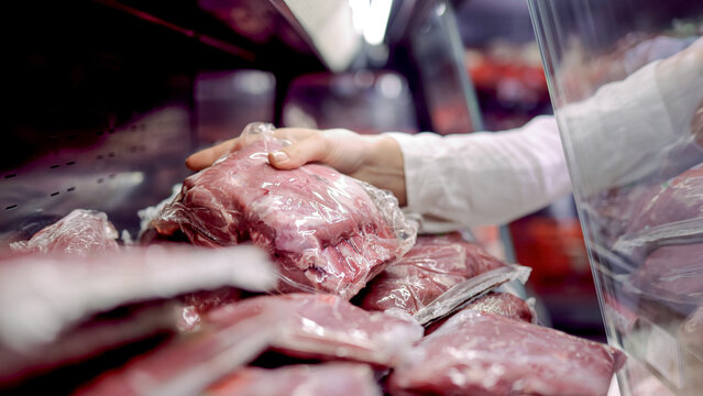 Fresh meat packages displayed in a grocery store refrigerator with a hand reaching for a selection, showcasing various cuts of beef in clear plastic wrapping