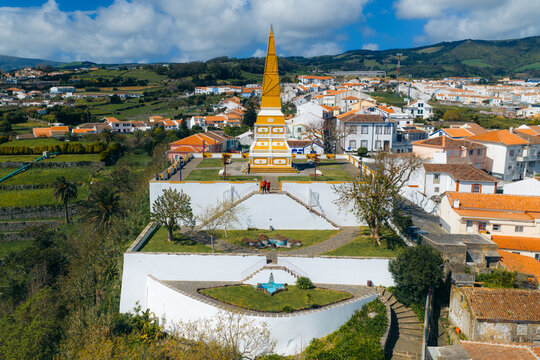 Aerial view of the Alto da Memoria monument with its yellow obelisk and tiered gardens overlooking the historic city and green hills Angra do Heroismo, Azores, Portugal.