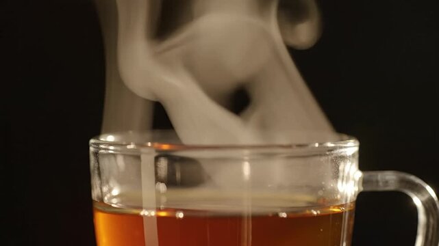 Teh Panas dalam Cangkir Kaca. Gambar menampilkan secangkir teh panas berwarna amber di dalam cangkir kaca bening dengan uap tebal yang naik ke atas, menghadirkan kesan hangat, segar, dan cocok dinikma