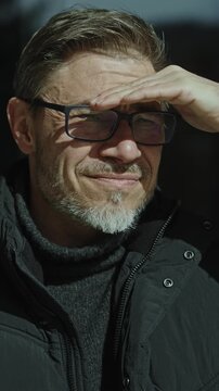 Middle aged man outdoor in front of wooden mountain home looking away to distance. Eyeglasses and gray hair. Happy satisfied smiling. Autumn clothing.