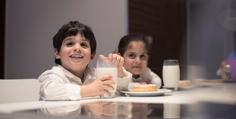 Obraz premium Middle Eastern family sharing iftar dinner at home with children drinking milk and enjoying donuts