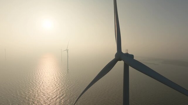Aerial drone view of offshore wind turbines in the sea covered in thick fog. Industrial wind farm generators in misty ocean water. Concept of renewable energy, foggy weather and green power.