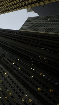 Buildings rise high in the city skyline at dusk. Lights shine from the windows, showing life inside. The darkening sky contrasts with the lights of the offices.