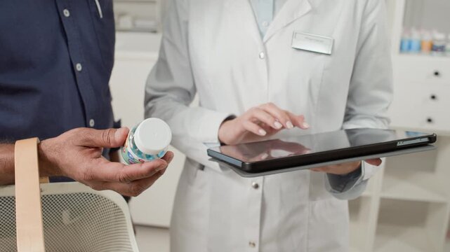 Close up shot of unrecognizable woman pharmacist using tablet while consulting male customer on medication ingredients in pharmacy, copy space