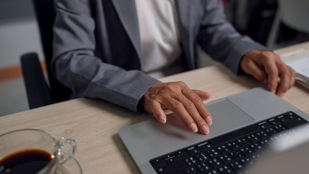 Hand rests gently on laptop trackpad. Finger tips poised, ready to navigate screens. Coffee cup beside, hinting at focused work. Professional attire suggests serious engagement