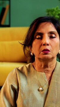 Indian senior couple doing omkar pranayama or yoga at home in the morning sitting with folded legs in modern living room chanting aum, practicing mindful breathing exercise for health