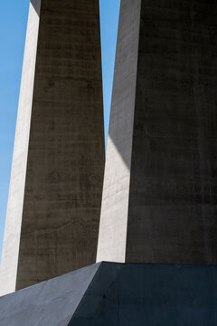 a concrete pillar rises between architecture walls, with shadow, urban structure, sky, exterior planes and geometric scale defining the vertical gap.