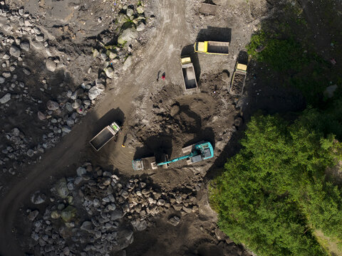 Aerial view of Tambang Pasir Merapi Kali Gendol Sand Mine with an excavator loading sand into trucks near rocks in Kecamatan Cangkringan, Daerah Istimewa Yogya, Indonesia.