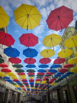 Colorful umbrellas suspended above the main street in Polczyn-Zdroj, Poland, creating a cheerful urban decoration against a blue sky. Vibrant travel scene from a small spa town with historic buildings