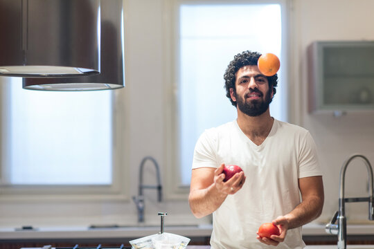 Middle Eastern man preparing iftar in a modern home kitchen while juggling fruit during Ramadan evening