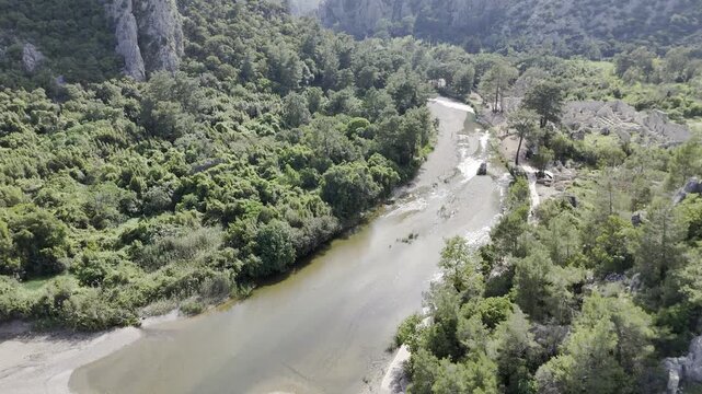 Aerial drone flyover of Cirali beach where the freshwater river meets the Mediterranean Sea. The footage features the scenic coastline, turquoise waters, and the overgrown ancient ruins of Olympos nes