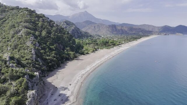 Aerial drone flyover of Cirali beach where the freshwater river meets the Mediterranean Sea. The footage features the scenic coastline, turquoise waters, and the overgrown ancient ruins of Olympos nes
