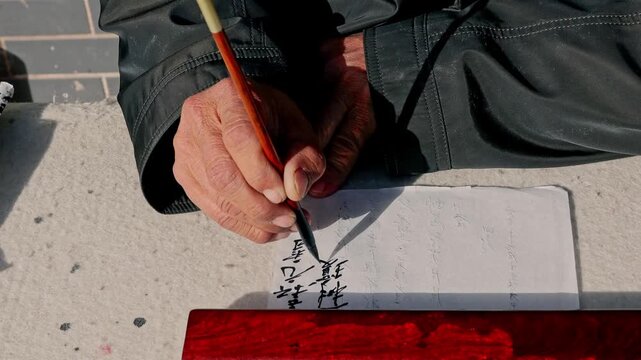 Elderly chinese calligrapher writing on paper with traditional brush