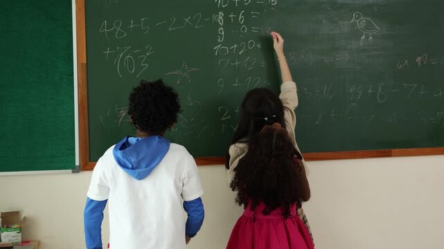 Three children writing math problems on a chalkboard in a classroom setting, engaged in learning and collaboration.