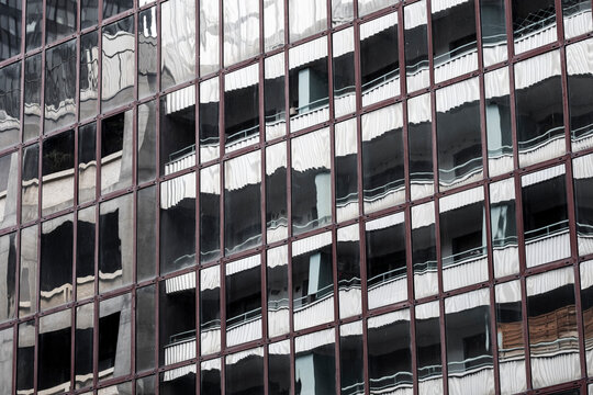 dark glass facade reflection repeats office windows across urban architecture, with exterior grid pattern and shadow bands running through the wall