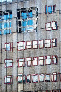 gray facade reflection surrounds blue windows on urban architecture, with red frames forming exterior pattern details across a concrete wall
