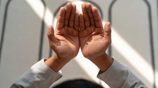 Close-up of human hands raised with open palms facing upward in a gesture of prayer or supplication under soft natural light and arched window background