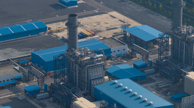 Aerial view of a large industrial power plant featuring tall chimneys and blue-roofed warehouses in Map Yang Phon, Rayong, Thailand.