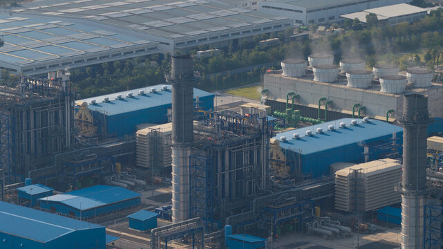 Aerial view of a large industrial power plant featuring cooling towers, tall chimneys, and blue-roofed warehouses Map Yang Phon, Rayong, Thailand.