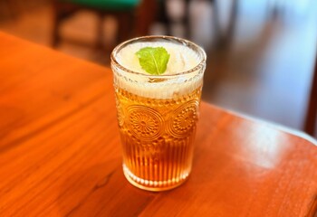 Golden Iced Beverage with Mint Leaf and Foam in Textured Glass on Wooden Table © suciramadhani