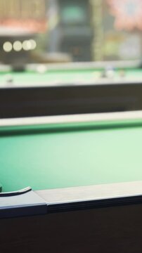 Two pool tables sit in a game room. Players focus on their shots while others watch. The scene shows balls scattered on the green felt. Friends gather for fun and competition.