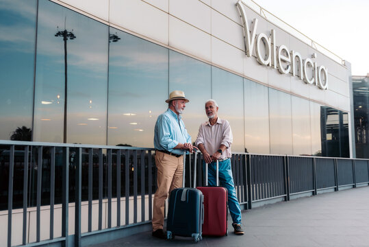 Two senior tourists standing with suitcases outside Valencia airport