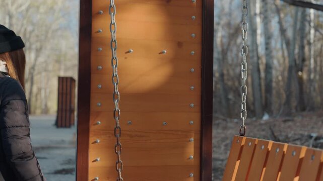 Caucasian woman at park bench, snatcher leans near wooden swing as abandoned plush toy waits winter light, backpack on shoulders, beanie, mask and gloves create furtive mood while closeup reveals toy