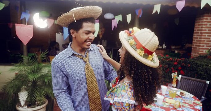 Joyful Brazilian couple dancing together at a traditional Festa Junina celebration wearing straw hats and colorful costumes under festive flags during a lively outdoor party event in Brazil