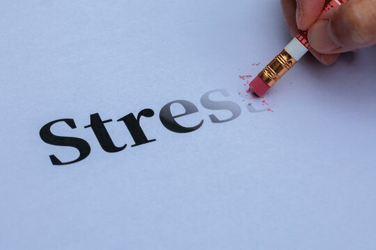 Hand erasing the word stress with a pencil eraser on white paper with copy space, close up concept of stress management relief mental health reduction relaxation and problem solving in everyday life
