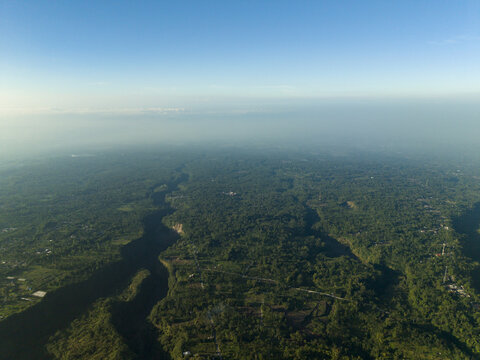 Aerial view of Kali Gendol river valley surrounded by dense tropical forests and rural settlements under a clear blue sky Cangkringan, Special Region of Yogyakarta, Indonesia.