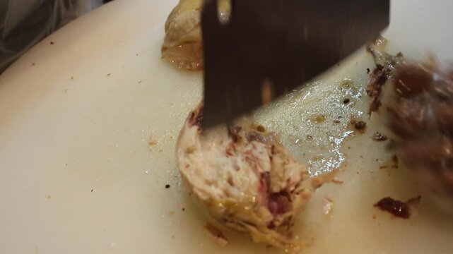 Chef chopping cooked chicken with a cleaver on white cutting board, close-up Asian restaurant kitchen food preparation
