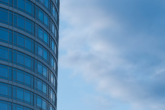 A blue glass facade curves beside the sky, letting urban architecture, windows and tower reflection carry exterior perspective through passing clouds.