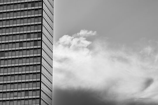 In black and white, clouds drift beside a tower facade as urban architecture turns windows, grid and vertical exterior lines into a graphic sky study.