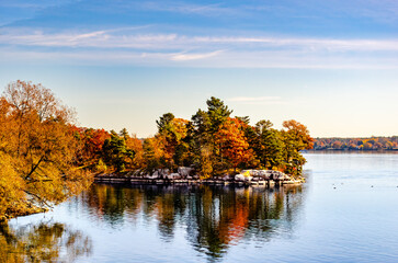 Obraz premium Rocky shored island on a river with bright autumn colored trees.