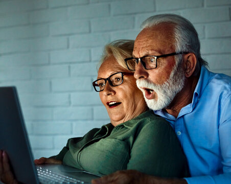 Portrait of an edlerly senior aged couple using laptop at night, watching tv together at home. Shot of a mature couple resting on the couch watching scary movie movie on a laptop, shocked, surpised te
