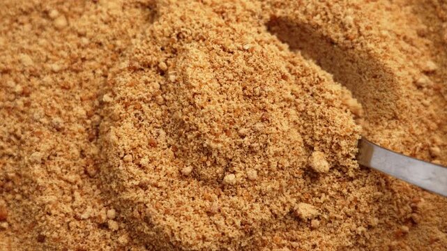 Scooping brown cane sugar with metal spoon. Golden granulated raw crystals. Top view