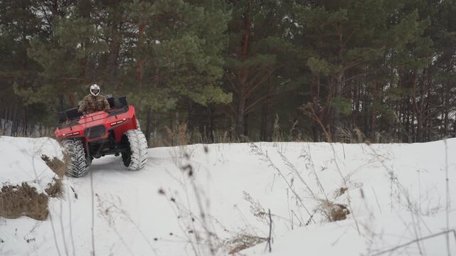 Red atv climbing steep snowy slope, helmeted rider in camouflage attacks crest, wheels churn snow and mud, close camera angle captures spray and engine roar, intense offroad challenge atmosphere