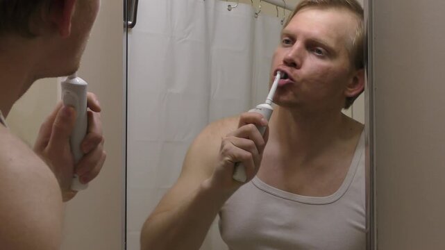 A white man brushing teeth with  electric toothbrush cleaning washes