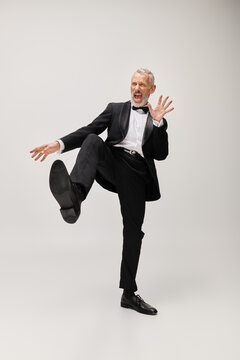 Elegant bearded man in a tuxedo dancing joyfully in a modern grey studio setting