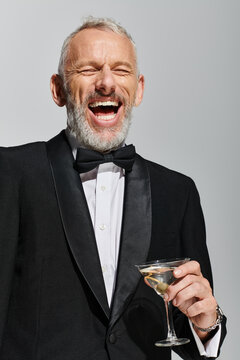Handsome middle aged man in tuxedo enjoying a cocktail in a stylish grey studio setting