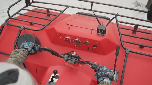 Helmeted rider on red atv dashboard, closeup of gloved hands on throttle and handlebar, gauges and cargo rack visible, packed snow underfoot, steady focused maneuvering for offroad utility run