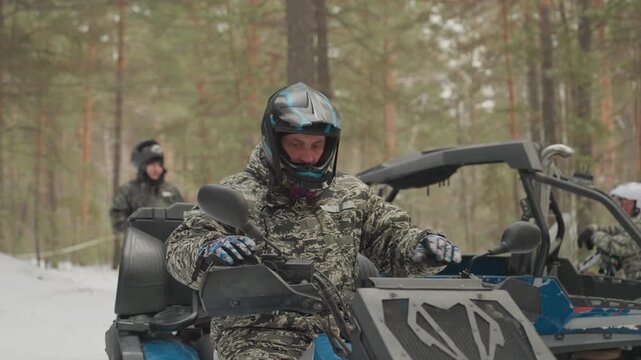 Caucasian man starts atv in snow adrenaline rider secures helmet and goggles, ignites blue utv, grips throttle, plunges into pine forest trail, engine roar and clouded breath, extreme winter ride