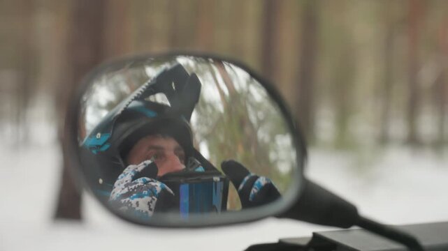 Snowy forest mirror closeup helmeted rider checking visor, rearview reflection captures focused gaze through goggles, teal black helmet detail, blurred pine background, calm anticipation