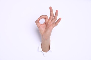 Naklejka premium Man showing ok gesture through hole in white paper, closeup