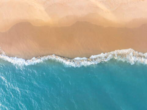 Peaceful aerial beach scene featuring blue ocean and warm sand shoreline. Minimal seaside background with space for text perfect for travel advertising and summer promotion visuals.