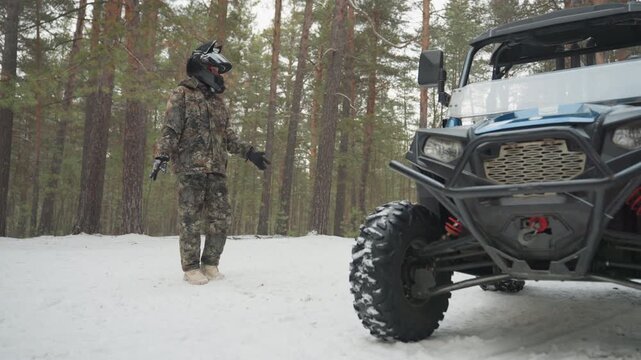 Camouflaged rider beside atv in snow, pine forest setting, rugged allterrain vehicle parked, rider inspects winch and front grille, full camo suit and helmet, snow packed tires, overcast light, quiet