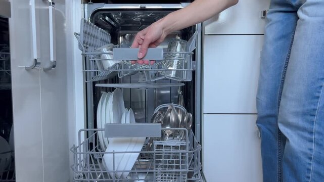 a modern kitchen setting featuring an open, built-in dishwasher packed with clean dishes. The loading or unloading process of the dishwasher.